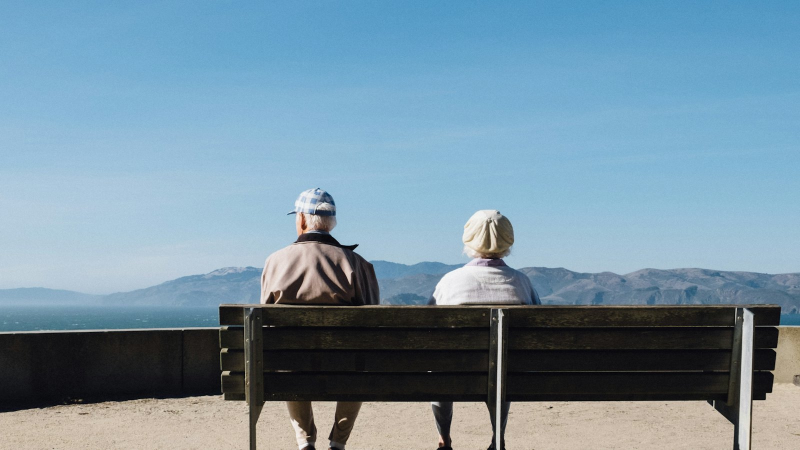A couple sitting on a bench looking out over the water toward the mountains