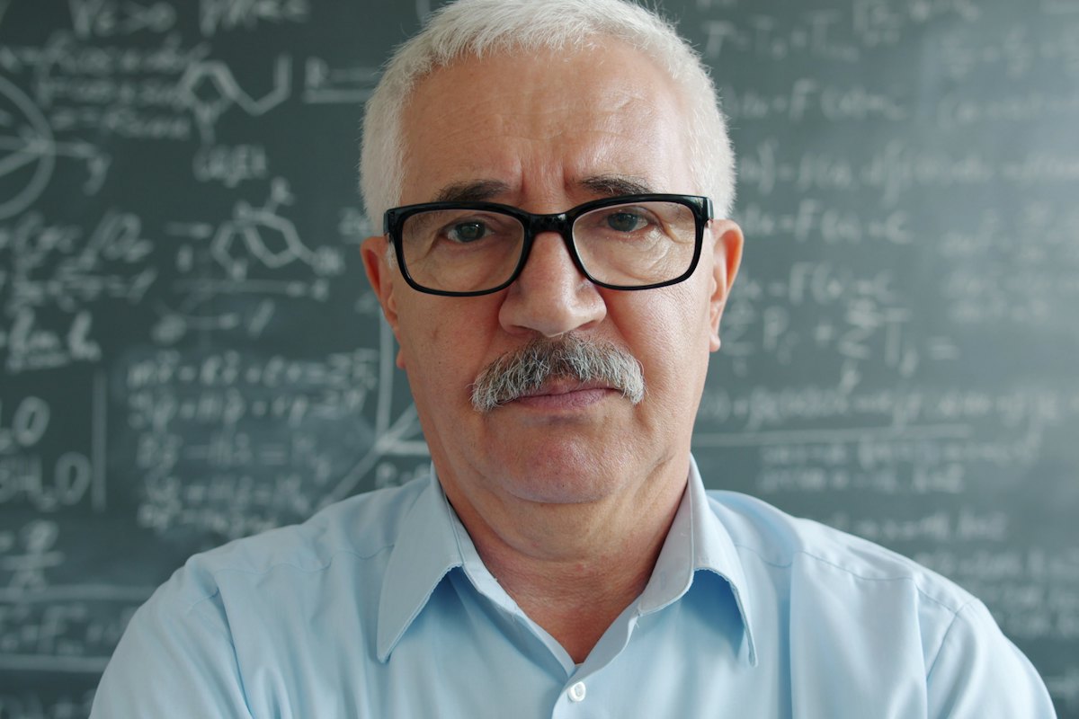 An older professor standing in front of a chalkboard